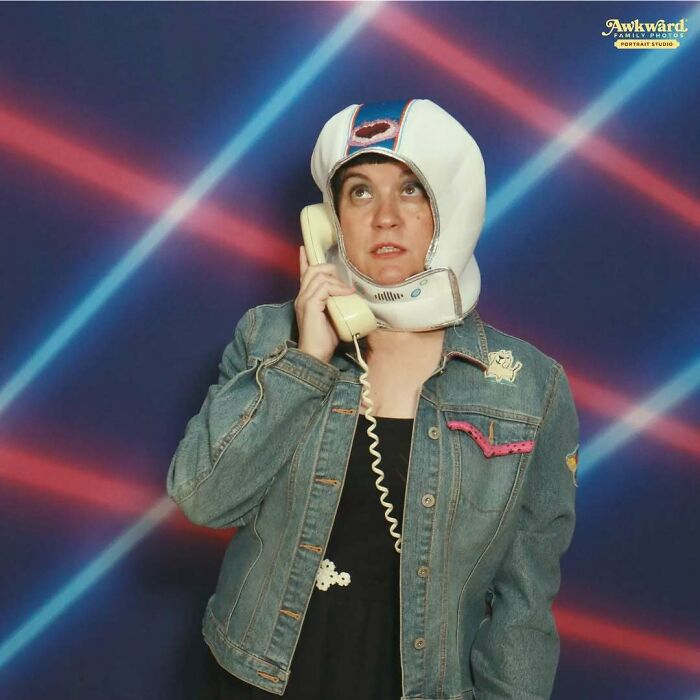 Person wearing a space helmet and denim jacket, holding a vintage phone in an awkward studio photo with neon lasers.