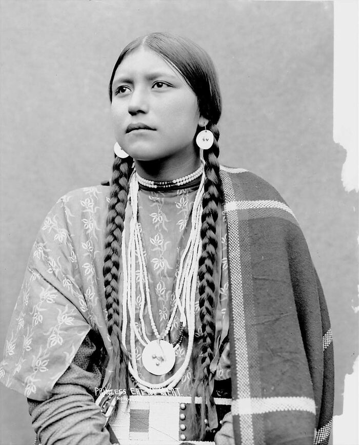 Victorian era portrait of a Native American woman with braided hair and traditional clothing in a black and white photo.