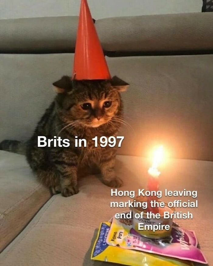 Cat wearing a cone hat next to a candle, humorously representing a history meme about Brits in 1997 and the British Empire.
