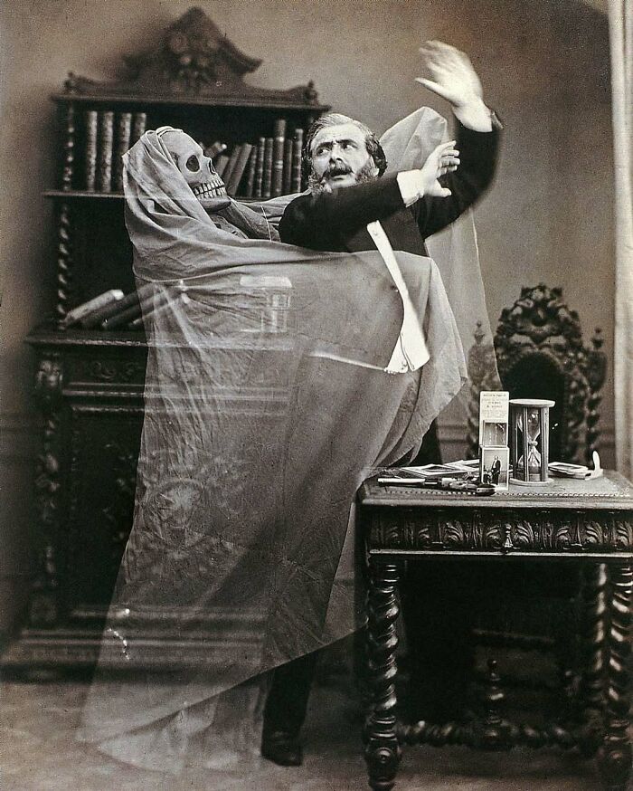 Victorian era weird photo of a man recoiling from a ghostly skeleton figure draped in a sheer veil inside a vintage room.