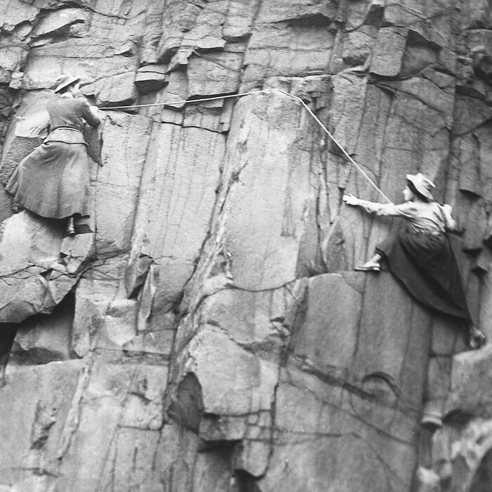 Two Victorian women climbing a steep rock face, showcasing unusual and adventurous activities from the Victorian era.