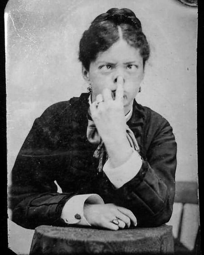 Victorian era weird photo of a woman making a funny face by pulling her nose with her fingers, black and white portrait.