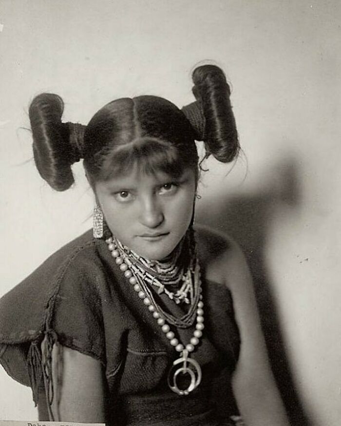 Victorian era woman with unique hairstyle and layered jewelry posing for a black and white vintage portrait.