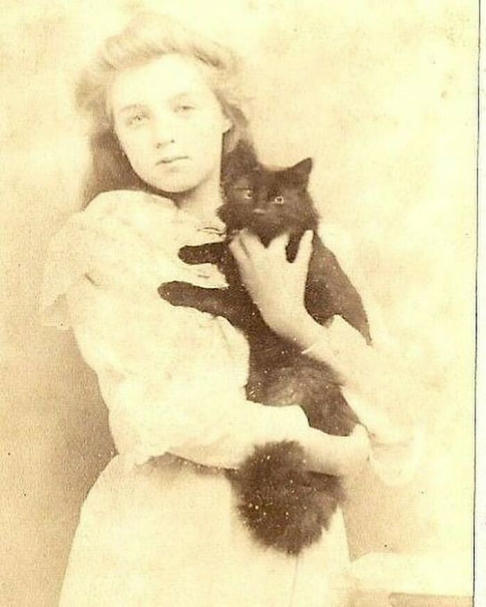 Victorian era photo of a young woman in white dress holding a fluffy black cat, showcasing weird Victorian era moments.