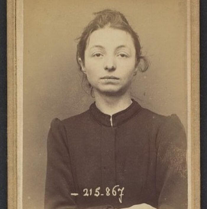 Victorian era mugshot style photo of a woman with serious expression wearing a dark high-collar dress.