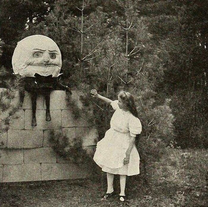Victorian era weird photo showing a young girl reaching toward a large Humpty Dumpty figure with a cat in an outdoor setting.