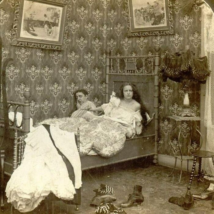 Victorian era weird photo showing a couple in bed with unusual outfits and a cluttered vintage bedroom setting.