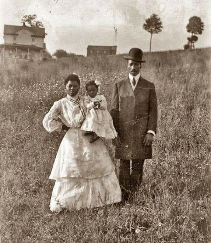 Victorian era family dressed formally standing in a field with vintage houses in the background, showcasing a different time.