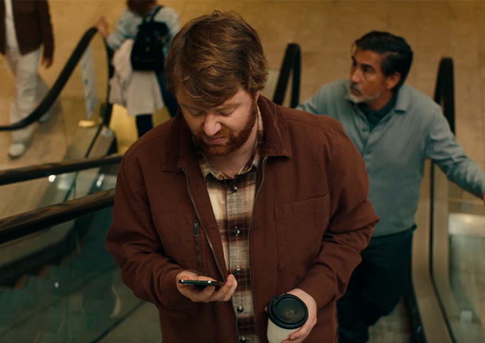 Man on an escalator looking at his phone, illustrating why parents shouldn't post about their children online in an ad. Man on an escalator looking at his phone, illustrating why parents shouldn't post about their children online in an ad.