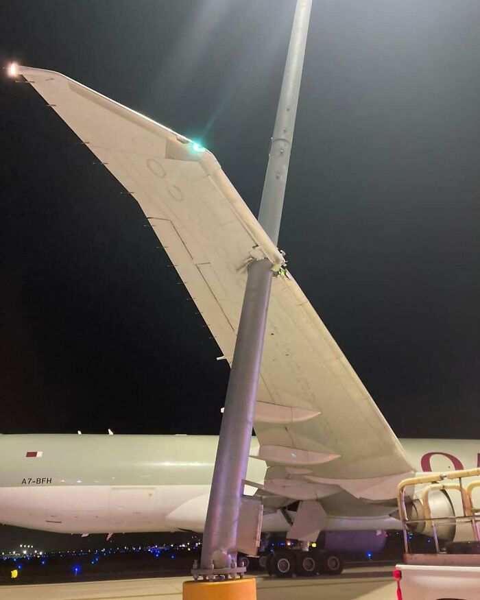 Airplane wing accidentally caught on a light pole on the tarmac at night, aviation memes inspiration for frequent flyers.