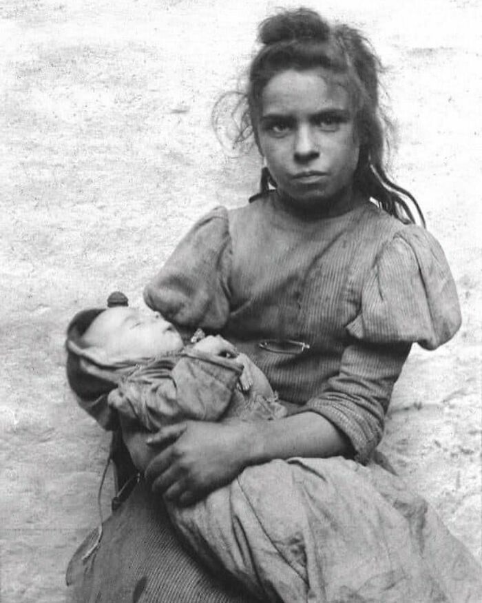 Black and white Victorian era photo of a girl holding a sleeping baby, illustrating the weird photos from the Victorian era.