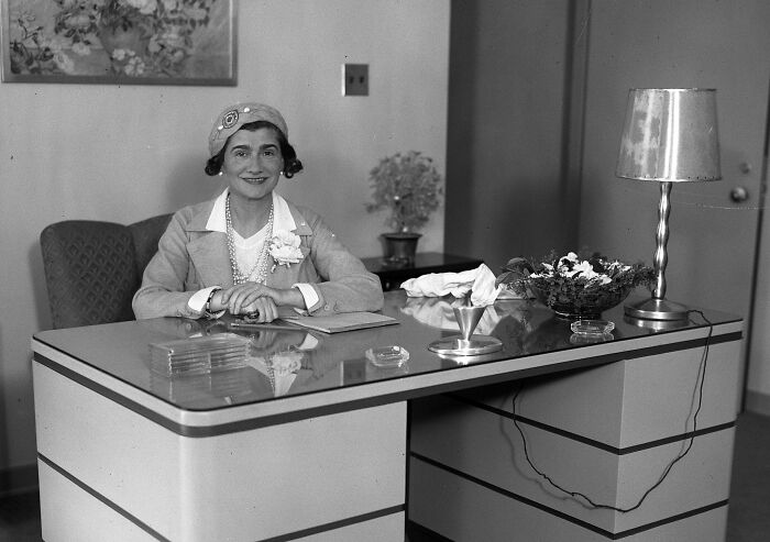 Classic style icon sitting at desk wearing a hat and pearls, illustrating timeless fashion influences on mood boards.