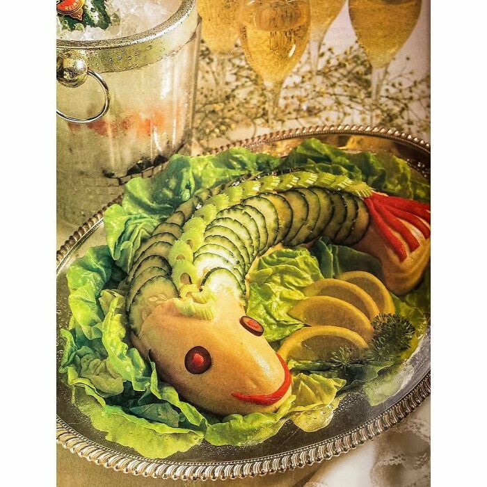 Vintage creative recipe platter shaped like a fish with cucumber, lettuce, lemon, and cranberry garnishes on a silver tray.