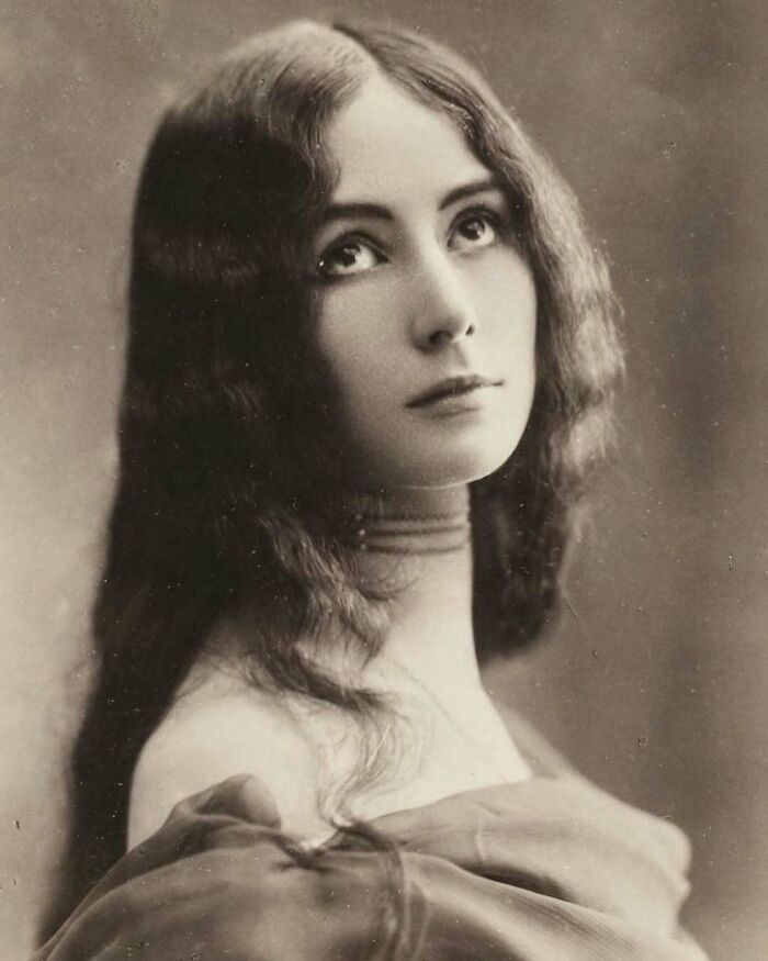 Victorian era portrait of a young woman with long hair looking up, showcasing fashion from a different time.