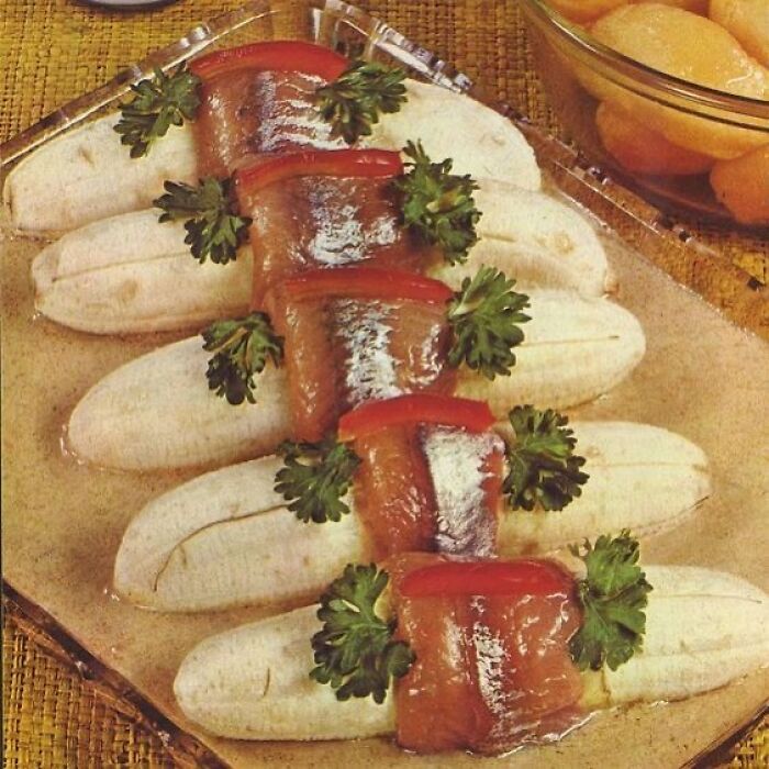 Vintage creative recipe featuring bananas wrapped with fish and garnished with parsley on a glass platter