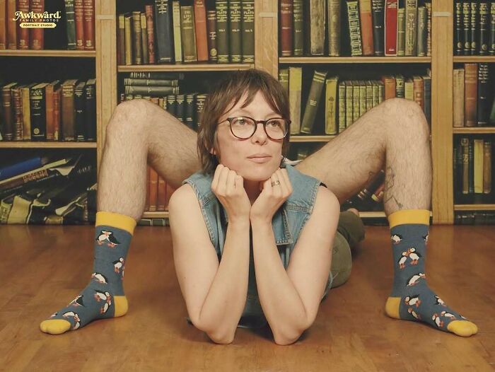 Woman with glasses posing in an awkward studio photo with a person in colorful socks and bent legs behind her.