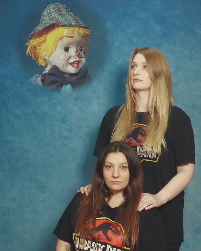 Two women wearing Jurassic Park shirts pose awkwardly in a studio with a floating clown head against a blue backdrop.