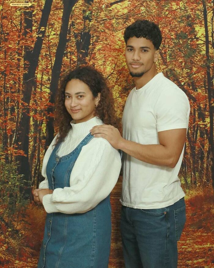 Young couple posing in a studio with an autumn forest backdrop, capturing awkward studio pics with casual outfits.