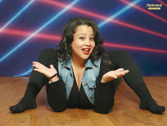 Woman in a denim vest and black outfit posing in an awkward studio pic with colorful laser light background on wood floor