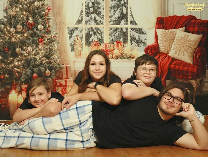 Family posing in an awkward studio photo with Christmas decorations and a cozy holiday backdrop.