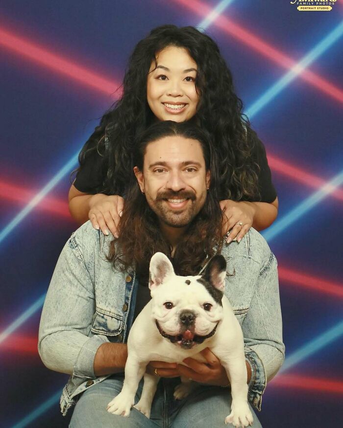 Couple posing with their dog in a studio portrait with colorful laser light background and awkward studio vibes.