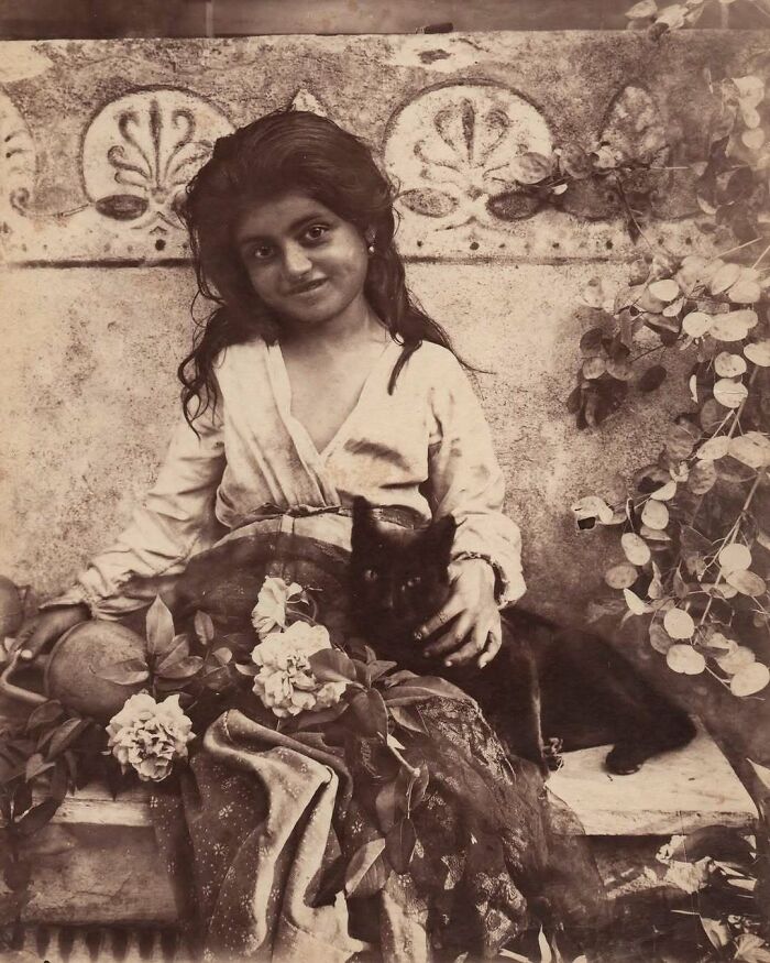 Victorian era photo of a young girl sitting with flowers and a black cat, showcasing weird photos from that different time.