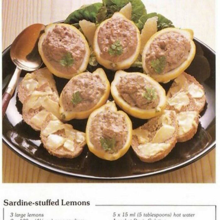 Vintage sardine-stuffed lemons served on a black platter with buttered bread slices, showcasing creative vintage recipes.