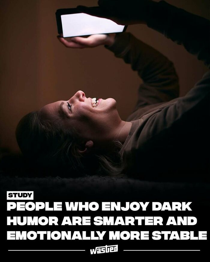 Person smiling while looking at a brightly lit mobile phone screen with fun facts and new things content.