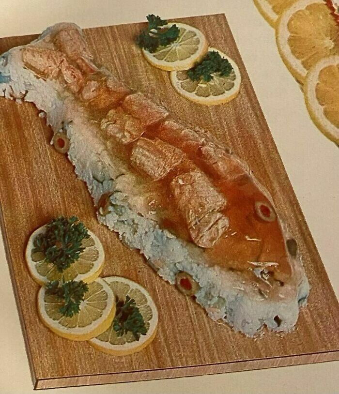 Vintage recipe of a whole fish molded with gelatin and garnished with lemon slices and parsley on a wooden board.