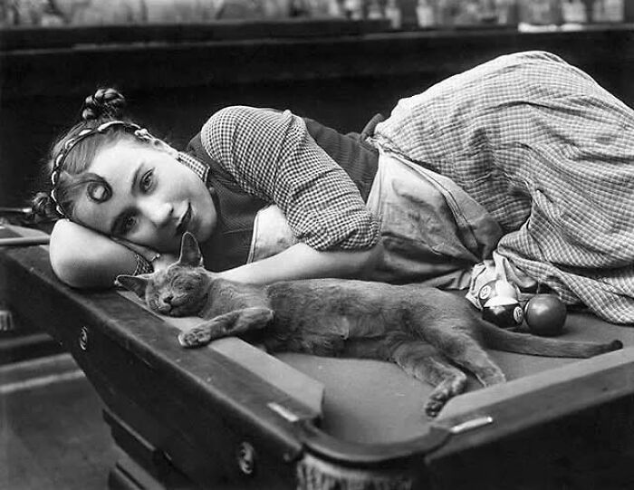 Victorian era photo of a woman lying on a pool table with a cat, showcasing the strange moments of that time.