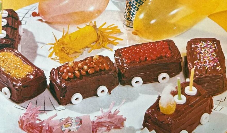 Vintage recipes featuring bizarre chocolate cake trains decorated with candy wheels and colorful toppings on a party table.
