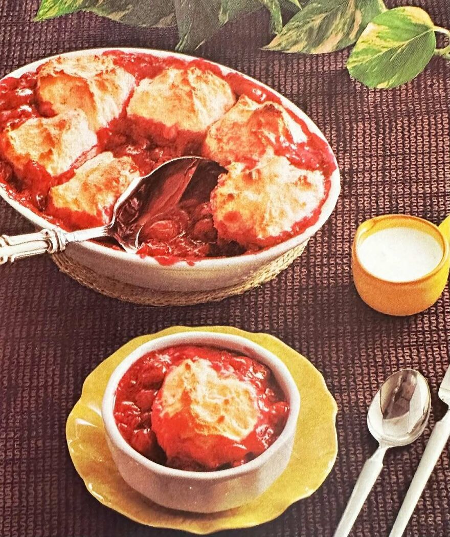 Vintage recipes dessert with baked biscuit topping and red fruit filling served in white bowls on a dark tablecloth.