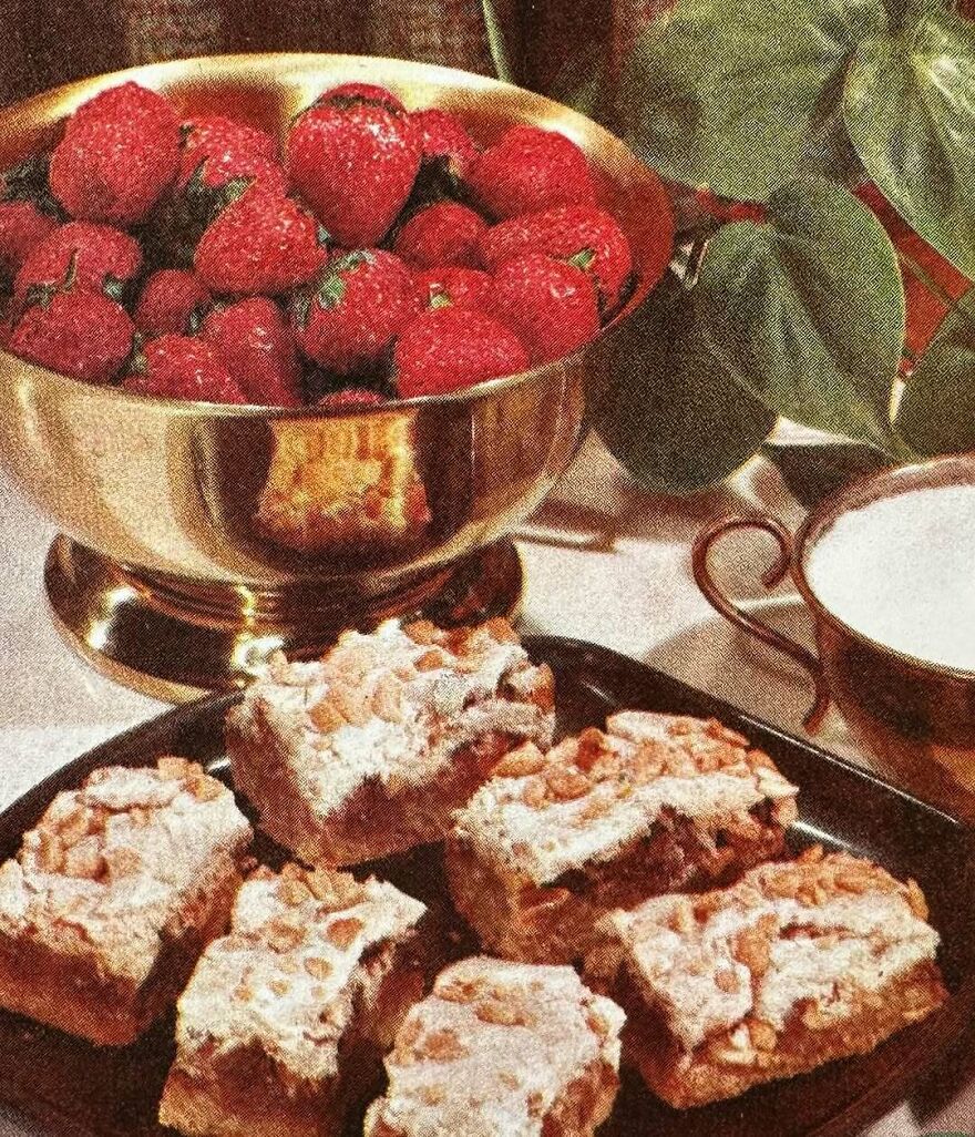 Vintage dessert bars topped with nuts served alongside a bowl of strawberries and a cup of milk on a table setting.