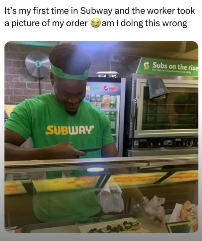 Subway worker wearing green shirt and visor taking a photo of a sandwich for a laughgorithm meme.