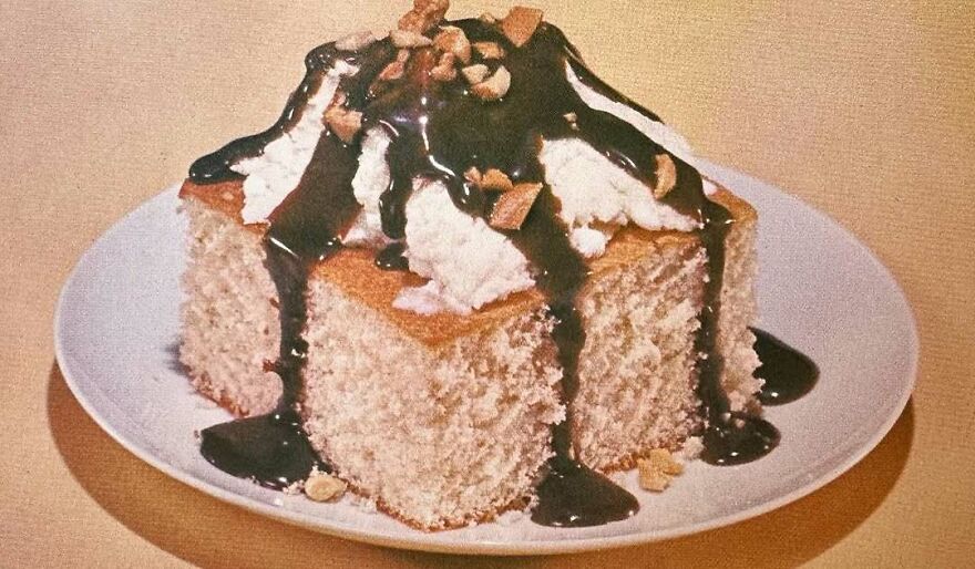 Vintage cake dessert topped with whipped cream, chocolate syrup, and nuts on a white plate showcasing vintage recipes.