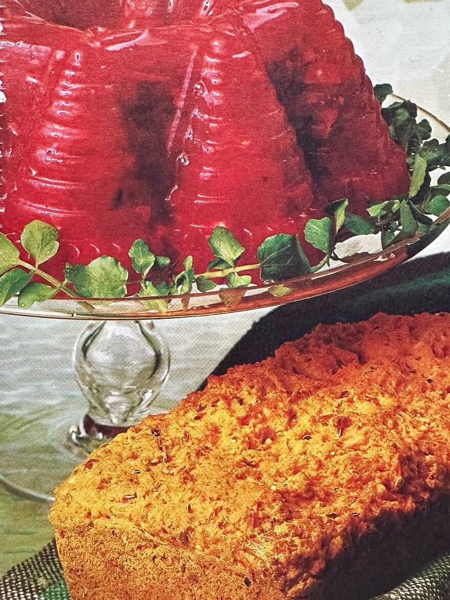 Vintage recipes showing a red gelatin mold on a glass stand and a textured loaf on a dark cloth.