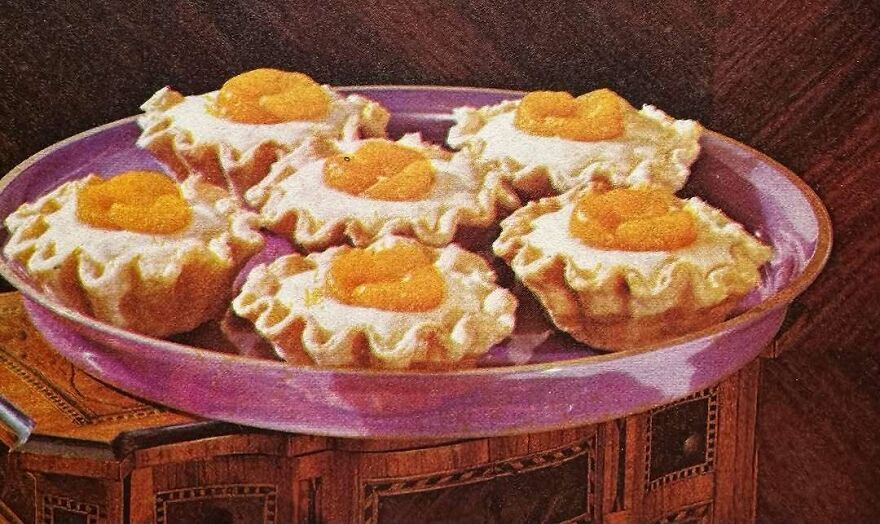 Vintage recipe featuring bizarre tartlets with creamy white filling and an orange topping on a purple oval plate.