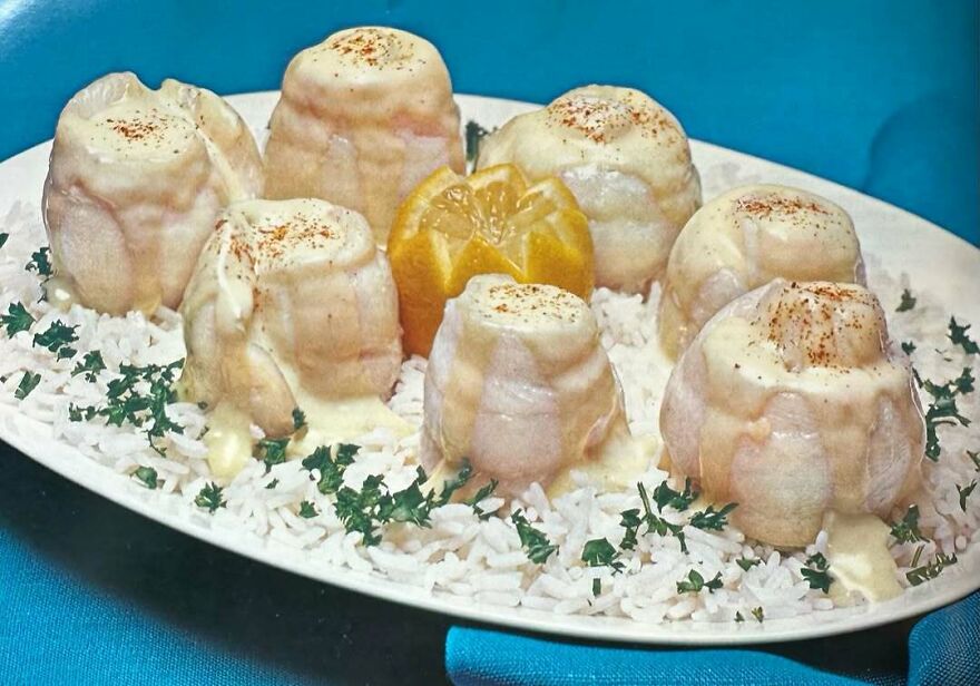 Vintage recipes featuring bizarre molded dishes covered in creamy sauce, served on rice with herbs and lemon garnish on a white plate.