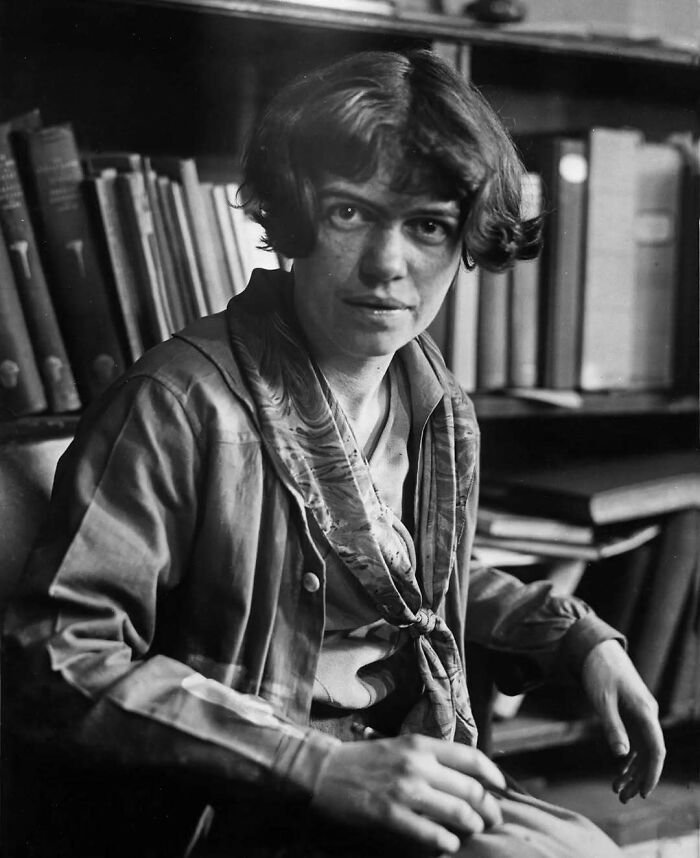 Black and white photo of a woman sitting near bookshelves, representing overlooked women in history and their achievements.