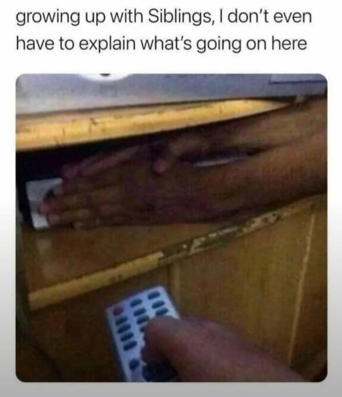 Hand hiding a remote control under a desk with caption about growing up with siblings, a funny meme for laughgorithm memes.