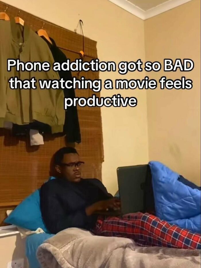Person in pajamas lying on bed using a laptop with a meme about phone a*******n to fight boredom and sadness.