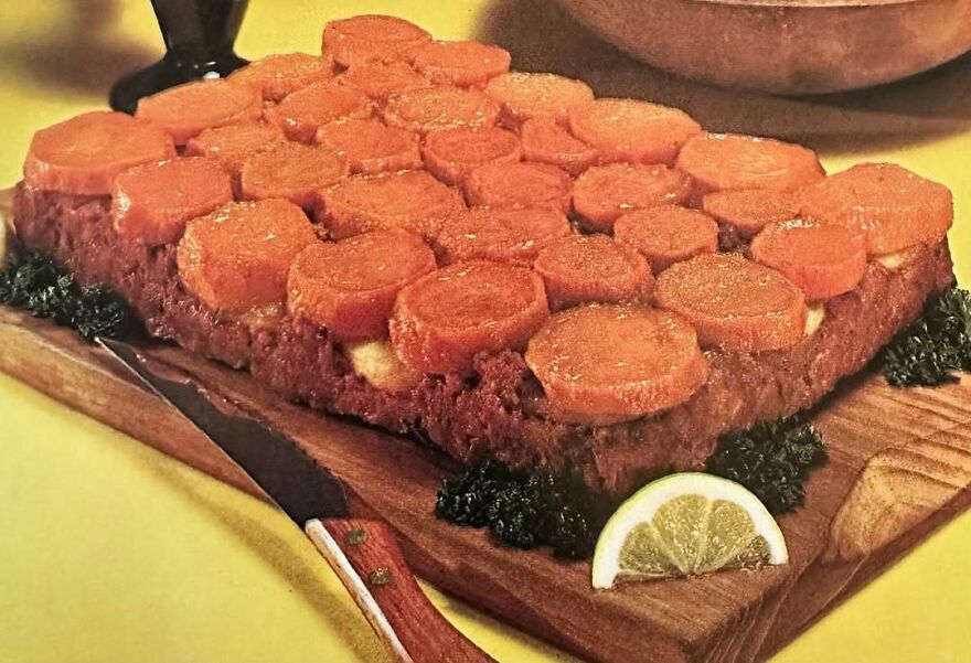 Vintage recipe featuring a meatloaf topped with cooked carrot slices, garnished with greens and lemon wedge on a wooden board.