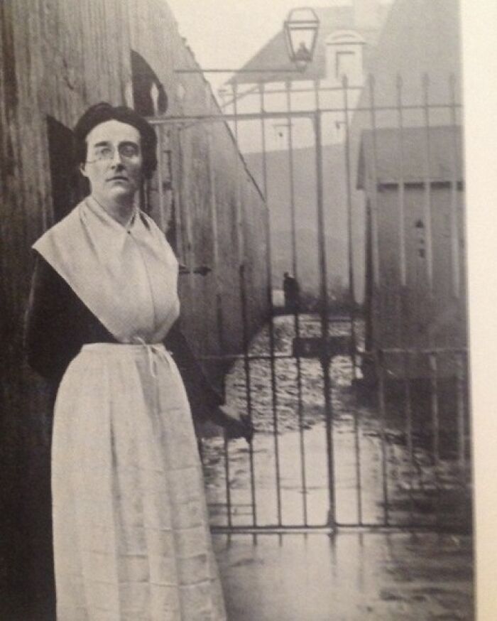Vintage photo of a woman in historical attire standing by a metal gate, representing overlooked women in history achievements.