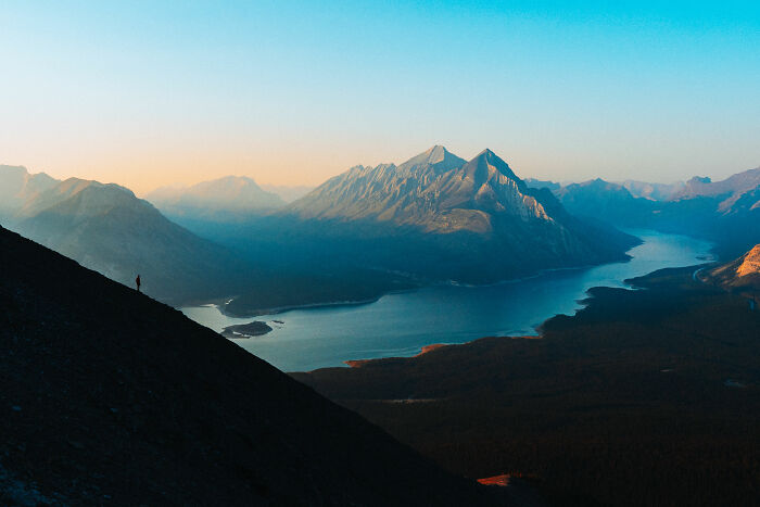 A lone hiker on a mountain slope overlooking a lake and distant peaks, symbolizing purpose and self-discovery.
