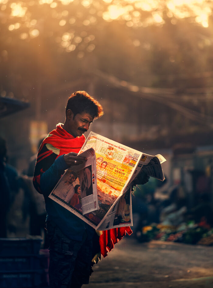 Man reading newspaper in warm street light, captured in vibrant street photography around the world.