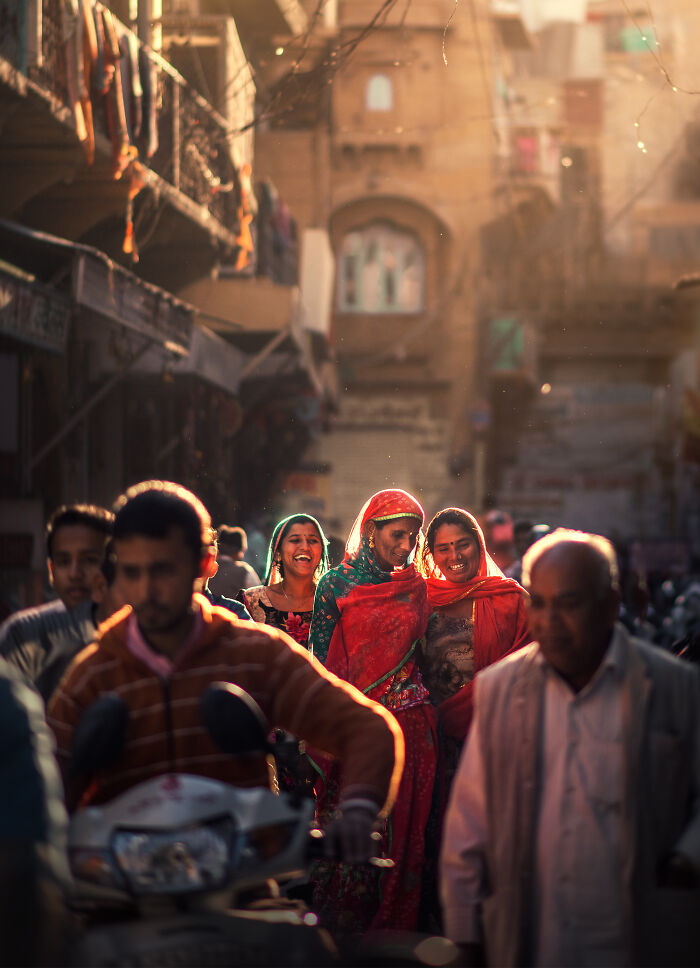 Street photography showing joyful women in vibrant dresses walking through a bustling sunlit urban street scene.