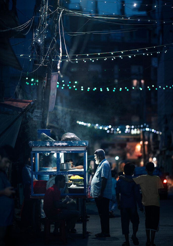 Street photography capturing a nighttime street food scene with people and colorful lights in an urban setting.