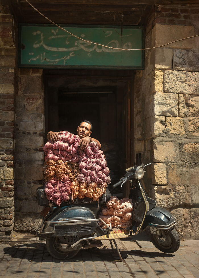 Man carrying bundles of yarn on a scooter in an old street during street photography around the world.