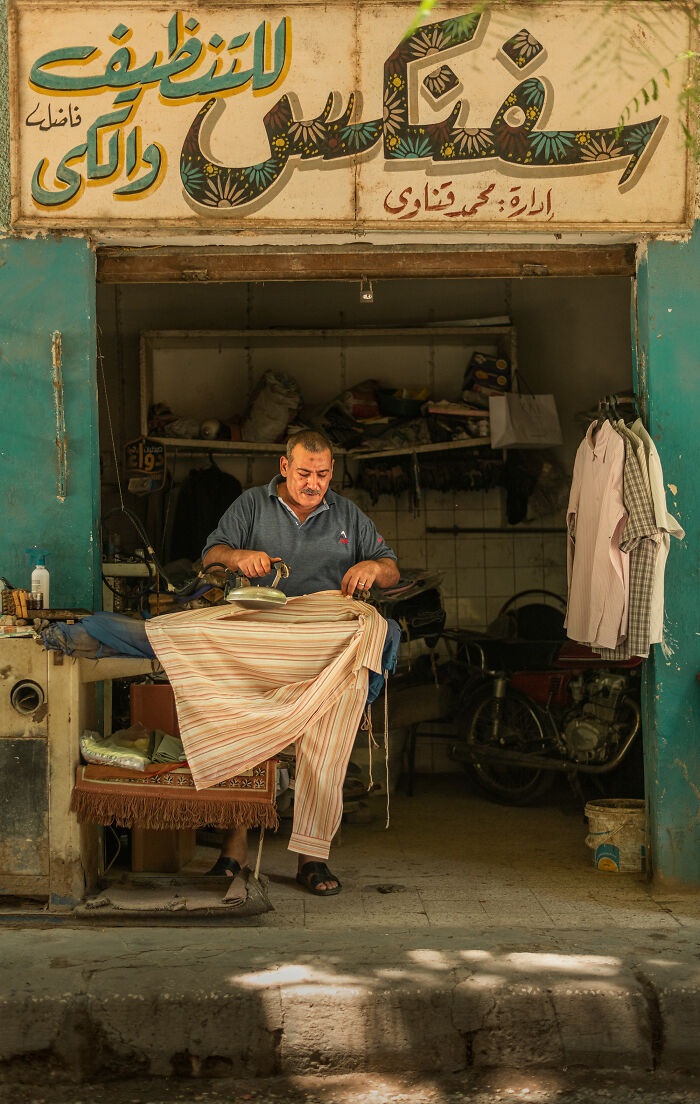 Man ironing clothes in a small traditional shop, captured in vibrant street photography around the world.
