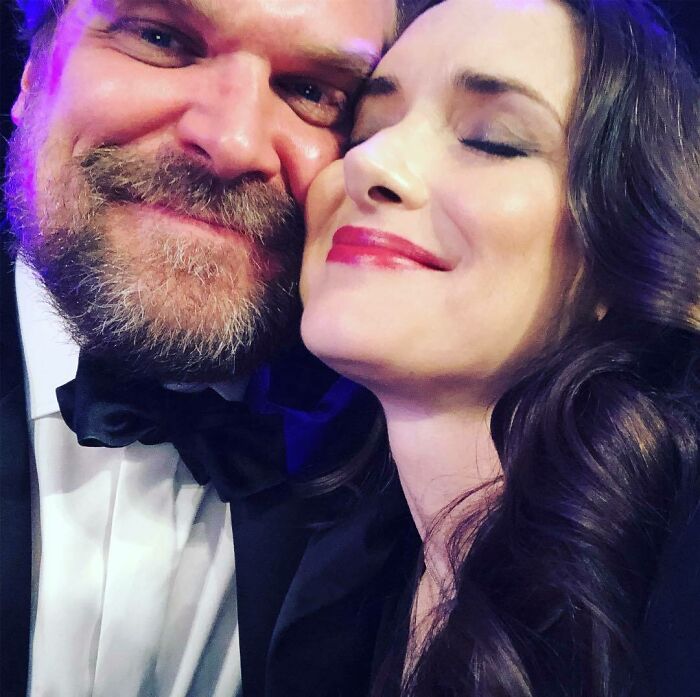 David Harbour and Stranger Things co-star close together, smiling and showing affection at a formal event.